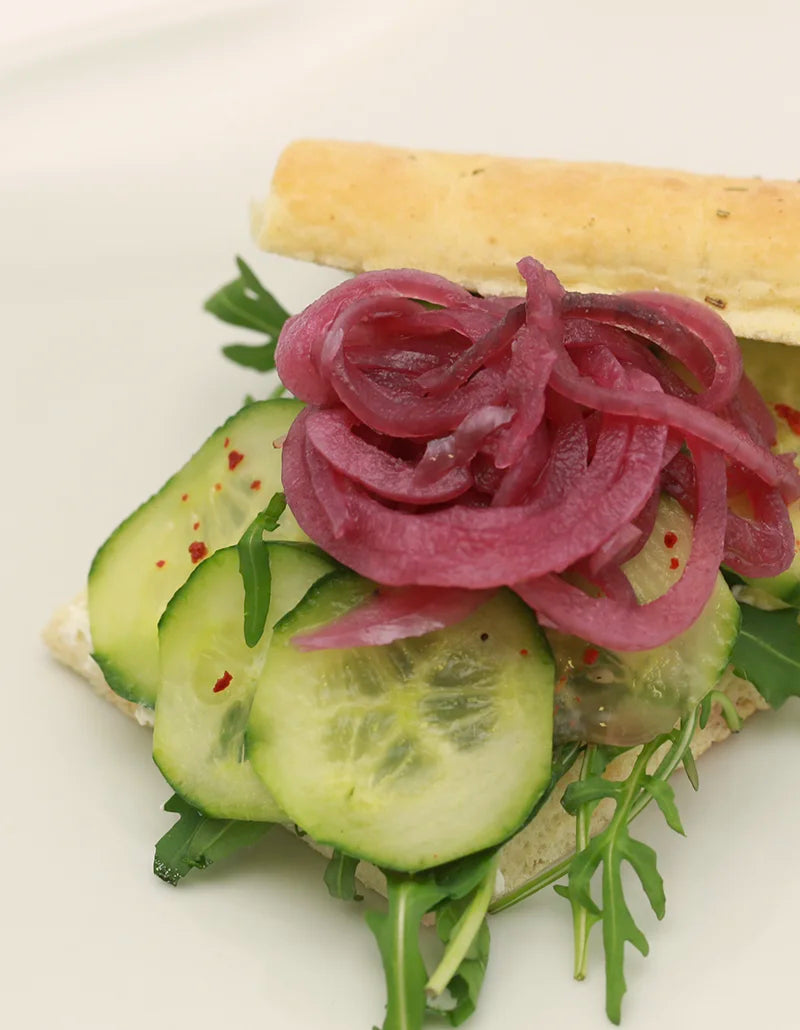 Belegtes Frühstücksgebäck mit Gurke, Rucola und eingelegten roten Zwiebeln