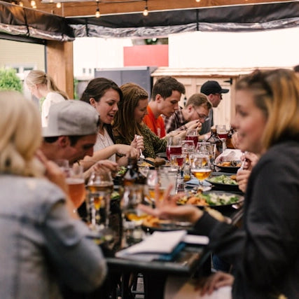 Gäste sitzen bei einer lockeren Firmenfeier gemeinsam an einer langen Tafel und essen.