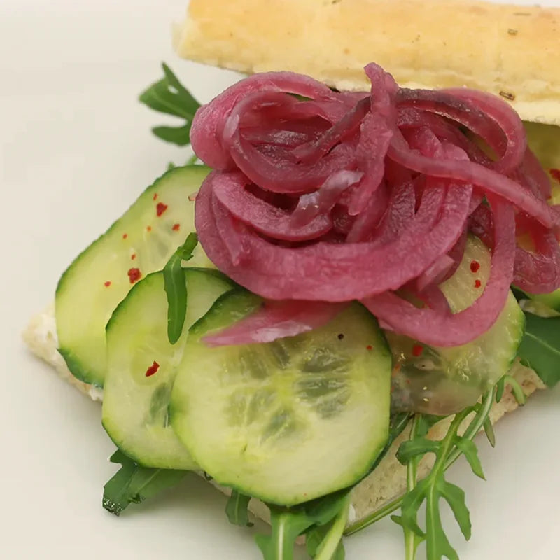 Belegtes Frühstücksgebäck mit Gurke, Rucola und roten Zwiebeln für das Standteam