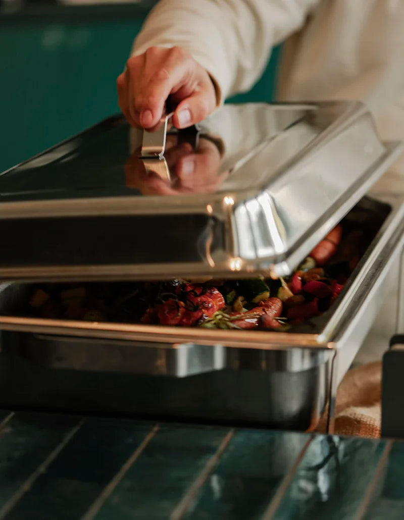 Person öffnet einen Chafing Dish mit warmem Gemüse für das Catering am Messestand